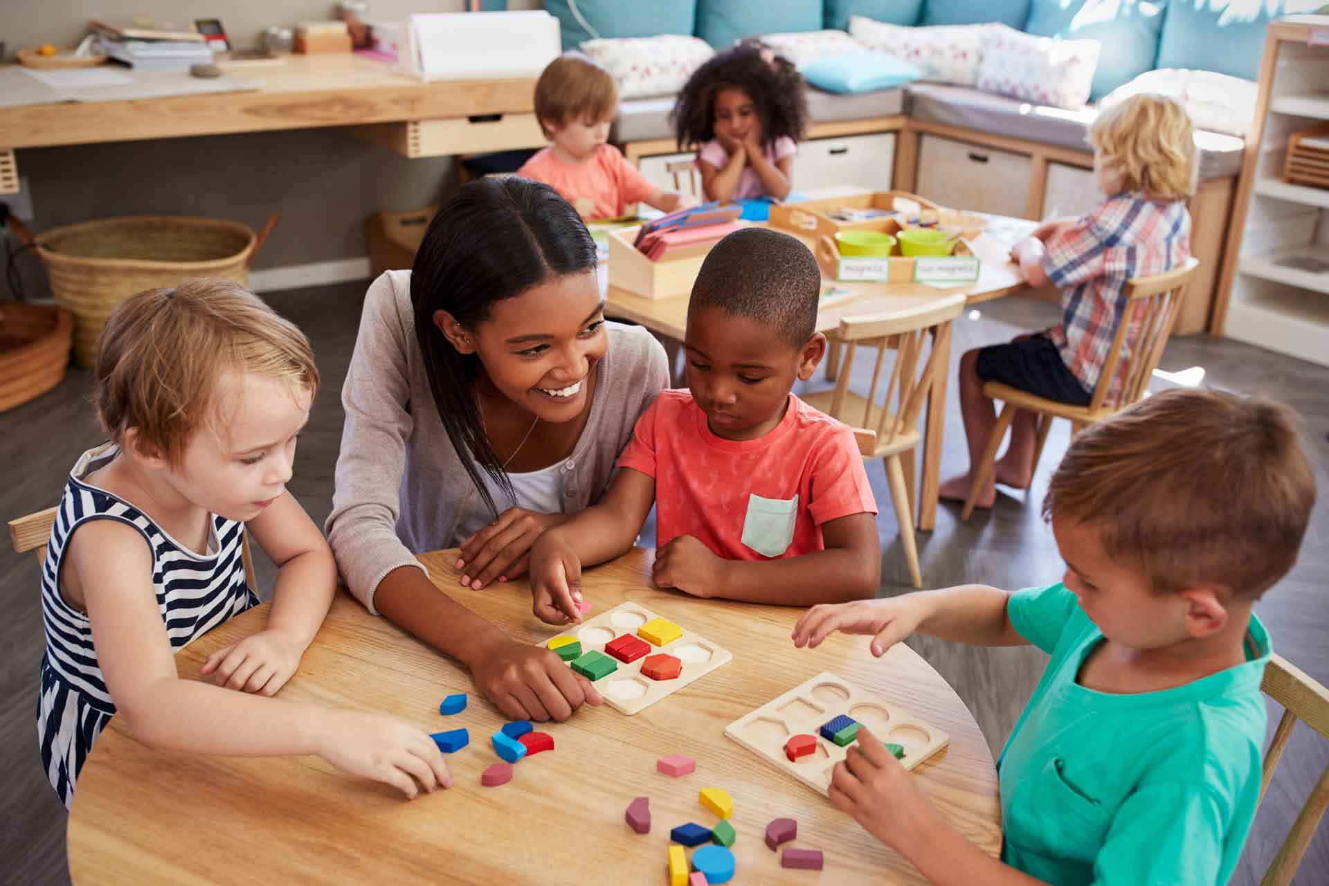 Teacher sitting at a table of small children with a wooden puzzle