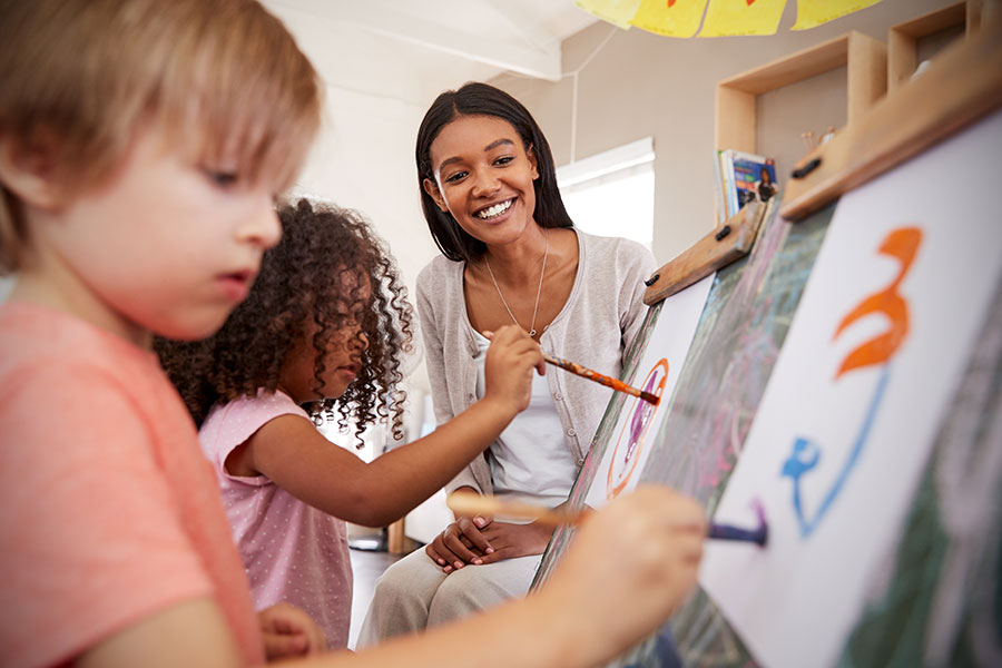 A teacher looking at 2 small children painting on easels