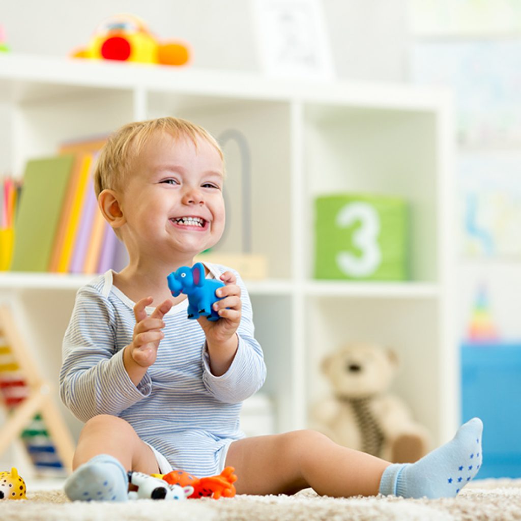 Toddler smiling and holding a blue elephant toy